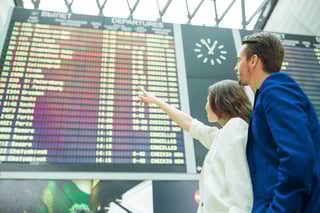Young Couple in International Airport Looking at the Flight Information Boar Young Couple in International Airport Looking at the Flight Information Boar